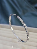 Silver bracelet with diamond accents on a white surface with a blue fabric background
