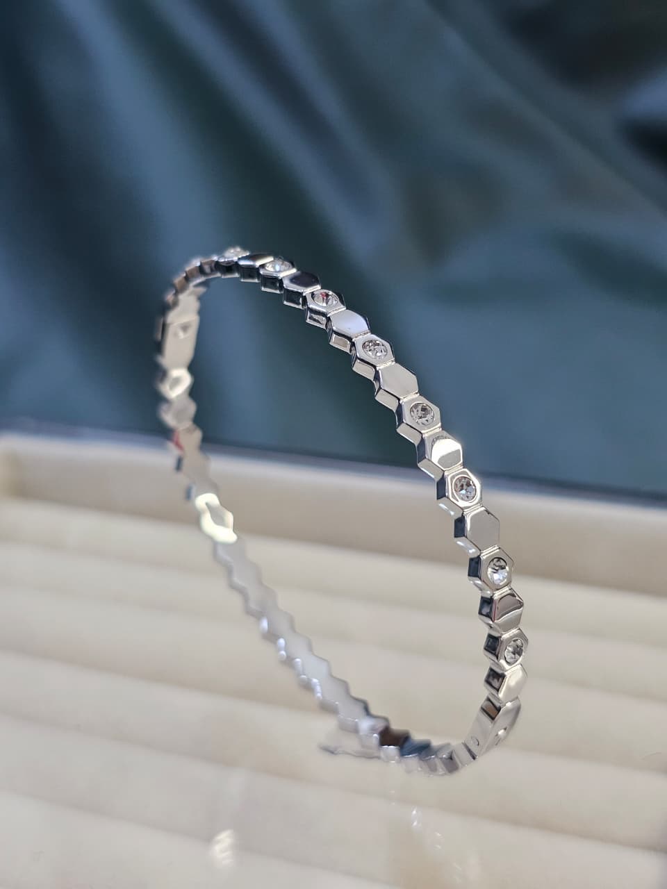 Silver bracelet with diamond accents on a white surface with a blue fabric background